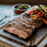 flank steak sliced into strips on a board with fajita toppings