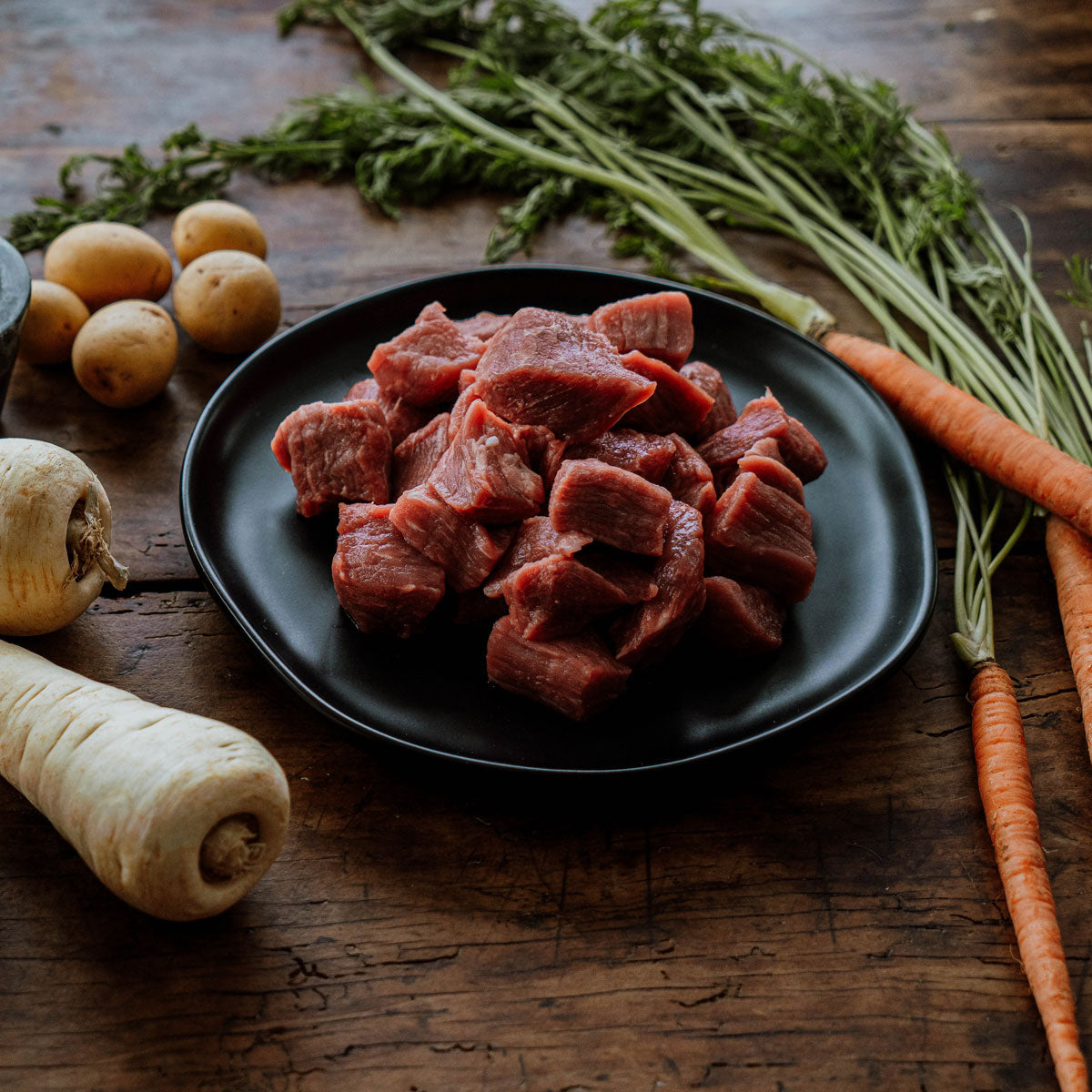 organic stew meat raw on a plate with veggies, prepping
